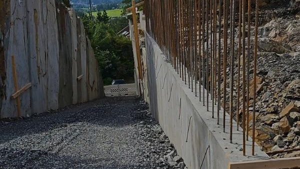 Ferdig støpt støttemur med armeringsjern på toppen, omgitt av stein og natur.